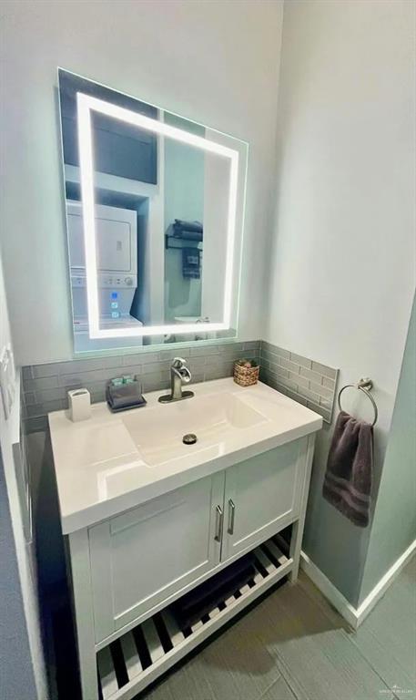 bathroom with stacked washer and dryer, baseboards, backsplash, and vanity