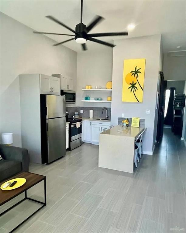 kitchen featuring a peninsula, a sink, a ceiling fan, white cabinets, and appliances with stainless steel finishes