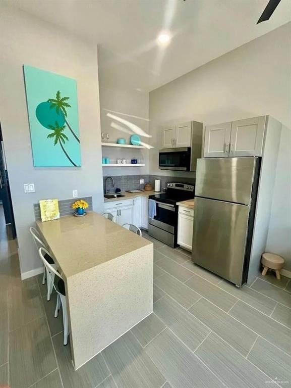 kitchen featuring a peninsula, white cabinetry, light countertops, appliances with stainless steel finishes, and a kitchen bar