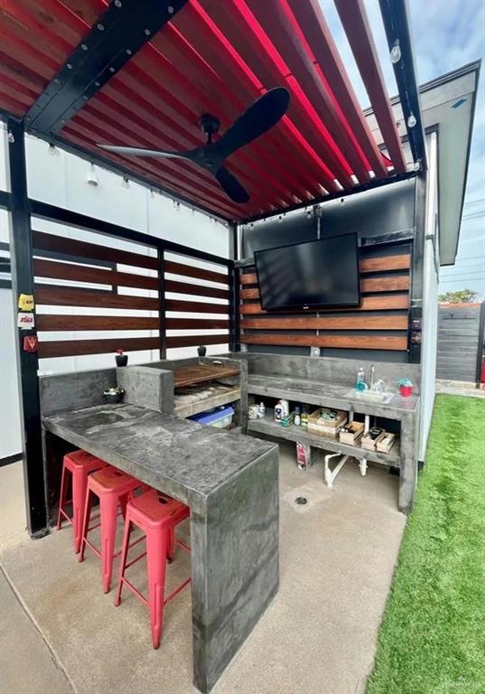 view of patio with ceiling fan, fence, and an outdoor bar