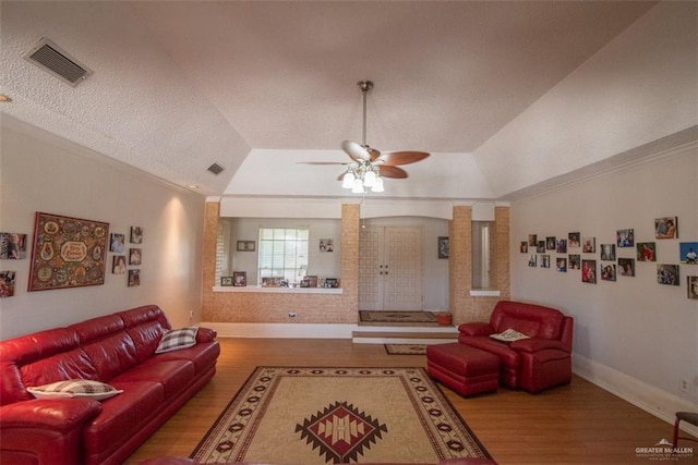 living room featuring decorative columns, ornamental molding, a raised ceiling, ceiling fan, and wood-type flooring