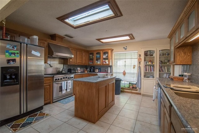 kitchen featuring a center island, wall chimney range hood, tasteful backsplash, light tile patterned floors, and appliances with stainless steel finishes