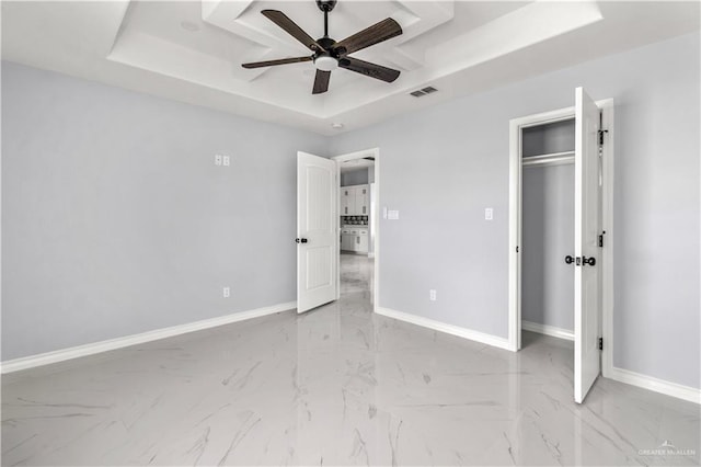 unfurnished bedroom with a tray ceiling, ceiling fan, and a closet