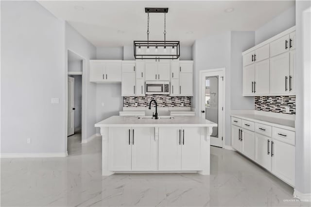 kitchen with white cabinetry, sink, hanging light fixtures, decorative backsplash, and a center island with sink