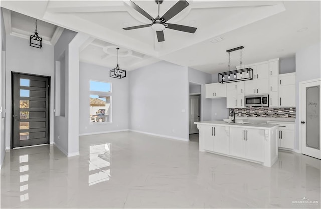 kitchen featuring tasteful backsplash, a kitchen island with sink, ceiling fan, white cabinetry, and hanging light fixtures