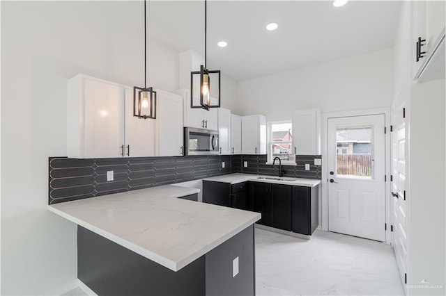 kitchen with white cabinetry, sink, hanging light fixtures, kitchen peninsula, and decorative backsplash