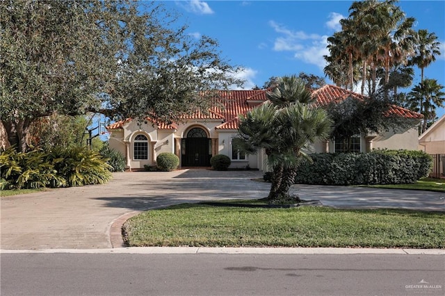 mediterranean / spanish house featuring a tile roof, decorative driveway, a front yard, and stucco siding