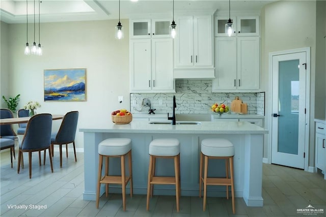 kitchen with decorative backsplash, a center island with sink, hanging light fixtures, and sink