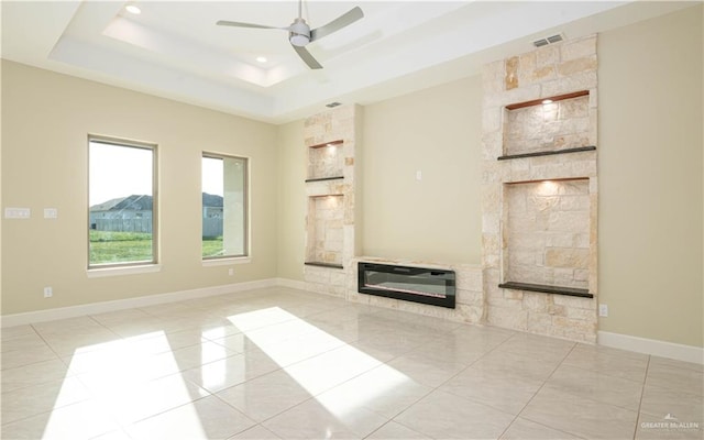 unfurnished living room with a fireplace, light tile patterned floors, a tray ceiling, and ceiling fan