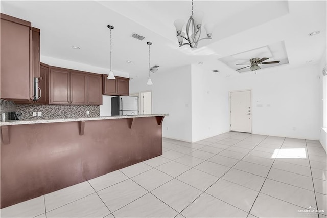 kitchen featuring white fridge, pendant lighting, a kitchen bar, decorative backsplash, and ceiling fan with notable chandelier