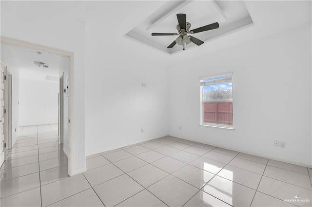 empty room featuring ceiling fan, a raised ceiling, and light tile patterned floors