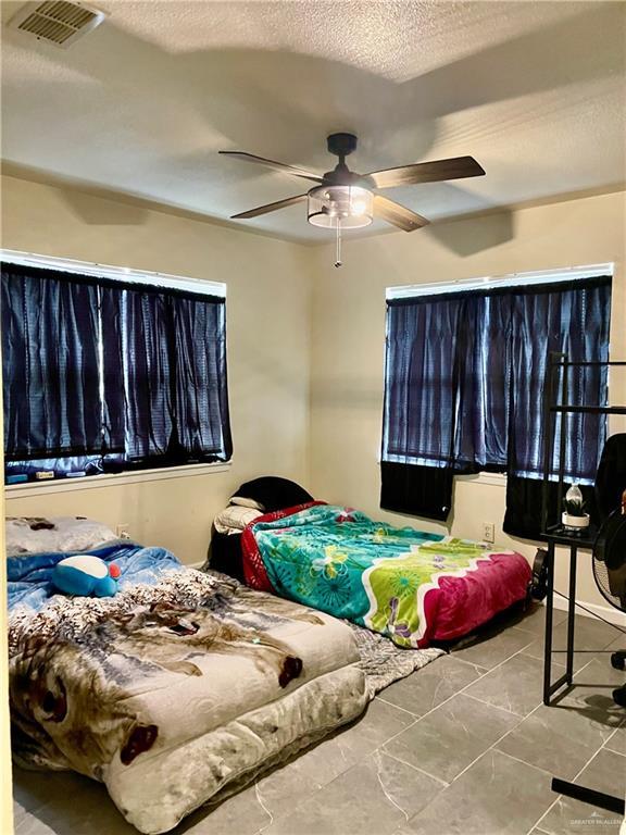 bedroom with a ceiling fan, visible vents, and a textured ceiling