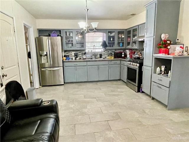 kitchen featuring a chandelier, gray cabinetry, a sink, appliances with stainless steel finishes, and glass insert cabinets