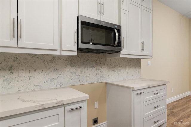 kitchen with light stone countertops, light wood-type flooring, and white cabinetry