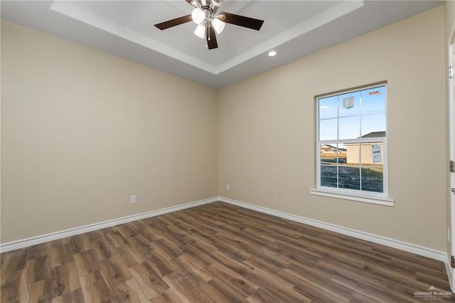 unfurnished room featuring a raised ceiling, ceiling fan, and dark wood-type flooring