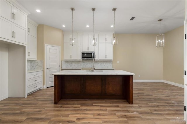 kitchen featuring decorative light fixtures, wood-type flooring, and a kitchen island with sink