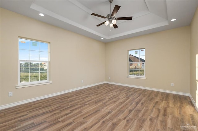 empty room with hardwood / wood-style floors, plenty of natural light, ceiling fan, and a tray ceiling