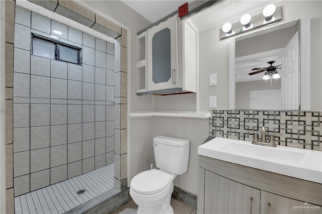 bathroom with decorative backsplash, a tile shower, vanity, ceiling fan, and toilet