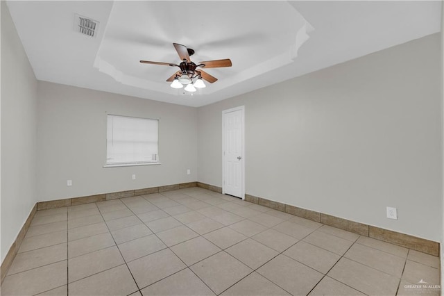 tiled empty room featuring a tray ceiling and ceiling fan