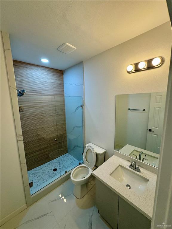 bathroom featuring a shower with door, vanity, and toilet