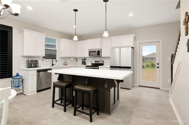 kitchen with white cabinets, hanging light fixtures, decorative backsplash, a kitchen island, and stainless steel appliances