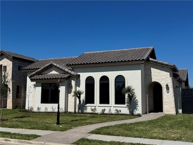 mediterranean / spanish home featuring stone siding, a tile roof, and a front lawn