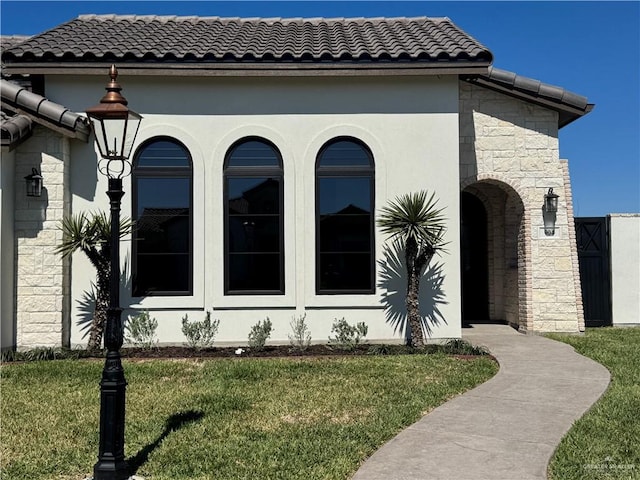 view of front facade featuring stucco siding, a tile roof, stone siding, and a front yard