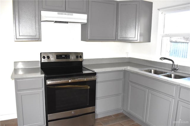 kitchen with wood finish floors, a sink, light countertops, stainless steel range with electric stovetop, and under cabinet range hood