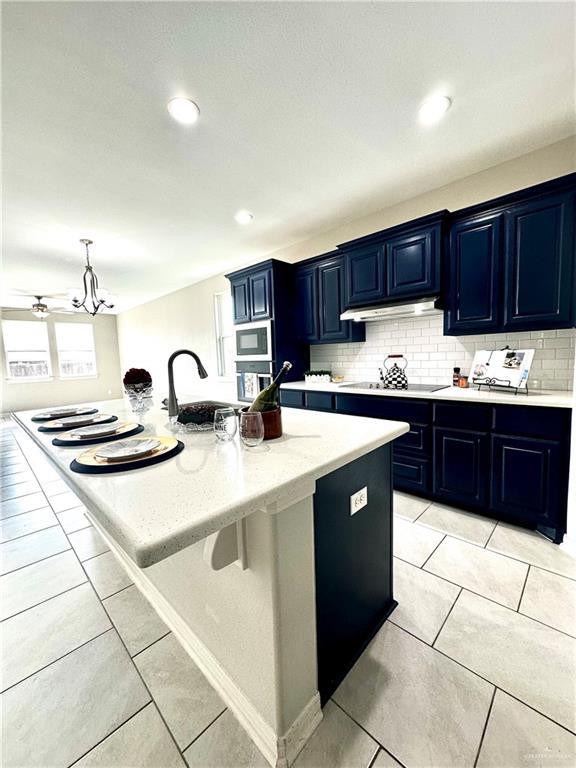 kitchen featuring light tile patterned flooring, blue cabinets, sink, decorative backsplash, and a center island with sink