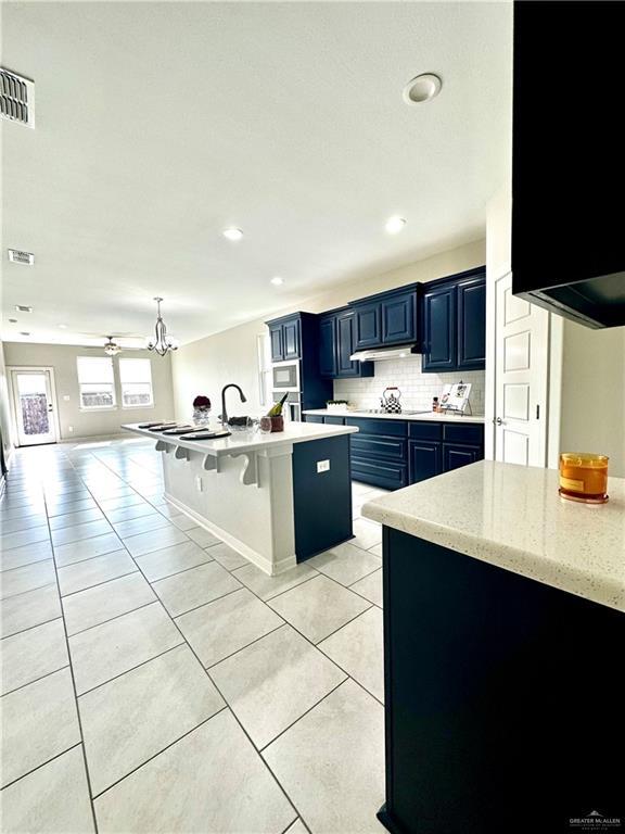 kitchen featuring blue cabinets, an island with sink, tasteful backsplash, a kitchen bar, and light tile patterned floors