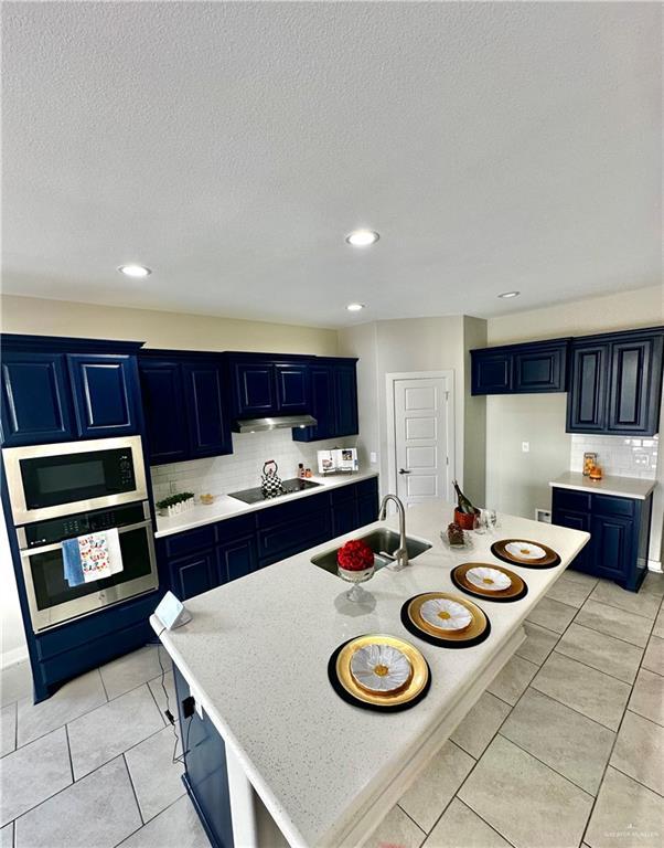 kitchen with blue cabinetry, appliances with stainless steel finishes, sink, and a kitchen island with sink