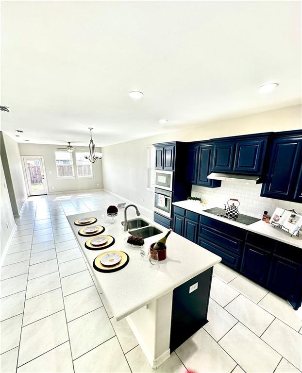 kitchen with blue cabinetry, a center island with sink, oven, and light tile patterned floors