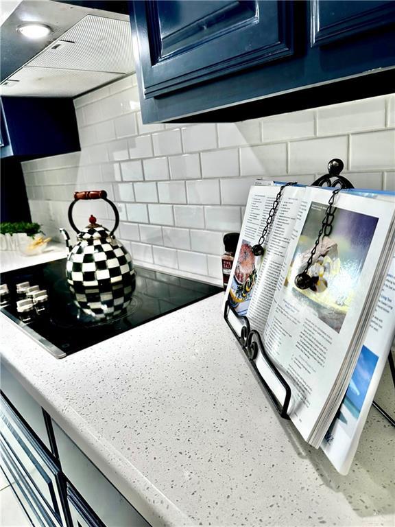 room details featuring black electric stovetop, decorative backsplash, wall chimney exhaust hood, and blue cabinets