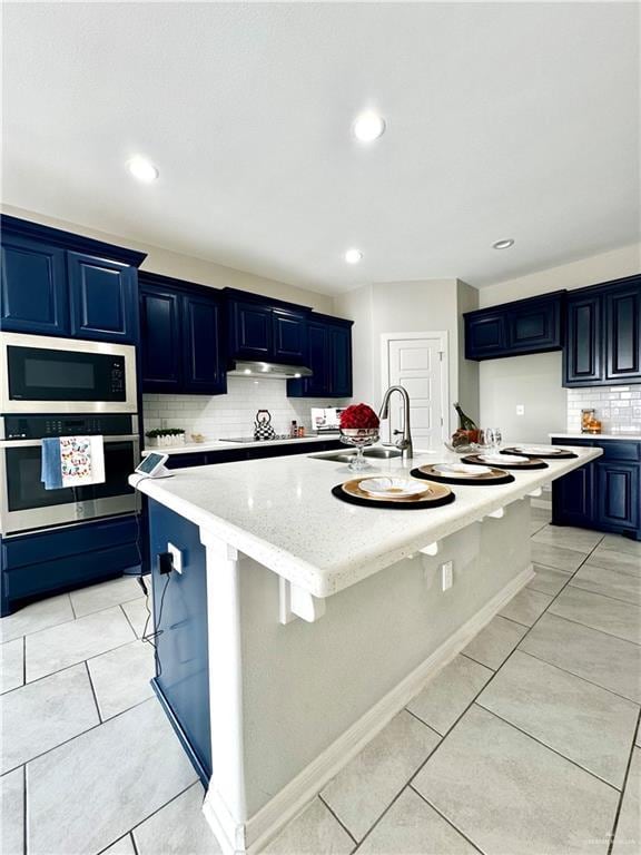 kitchen with tasteful backsplash, blue cabinets, light tile patterned floors, stainless steel appliances, and a center island with sink