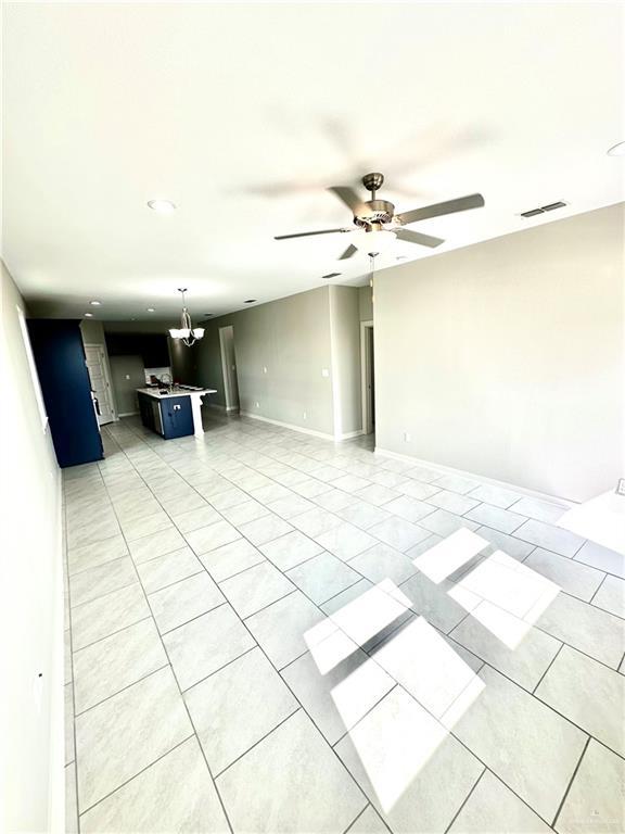 unfurnished living room featuring ceiling fan with notable chandelier and light tile patterned floors