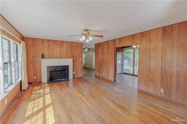1150 N Bowie St, San Benito, TX 78586 - unfurnished living room with light wood-style floors, wooden walls, a ceiling fan, and a tile fireplace