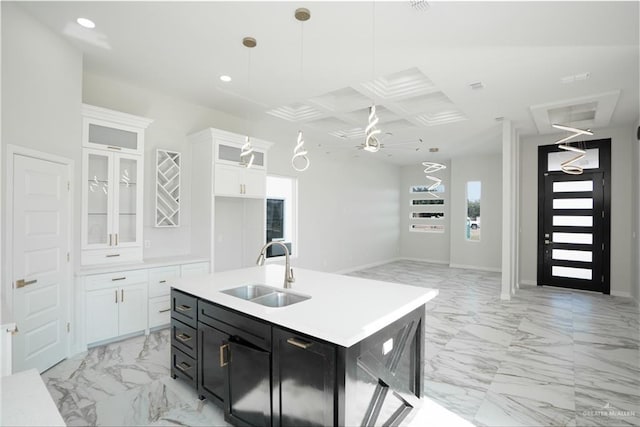 kitchen with white cabinetry, sink, hanging light fixtures, coffered ceiling, and a kitchen island with sink