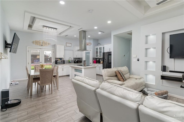 living room featuring a notable chandelier, a raised ceiling, sink, and french doors