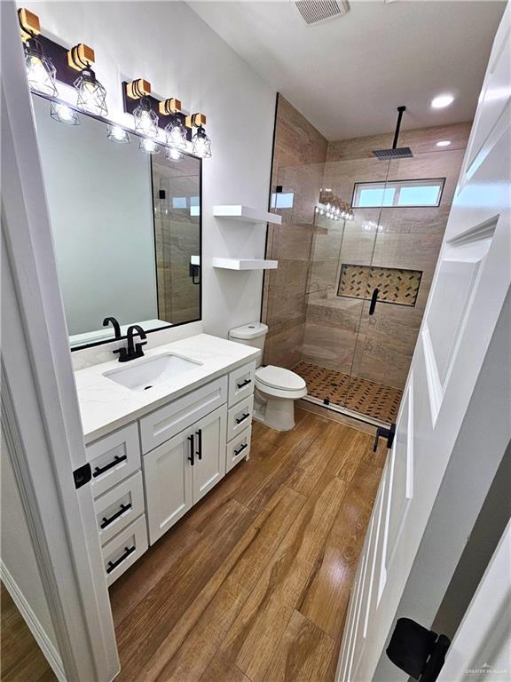 bathroom featuring hardwood / wood-style flooring, vanity, toilet, and a shower with shower door