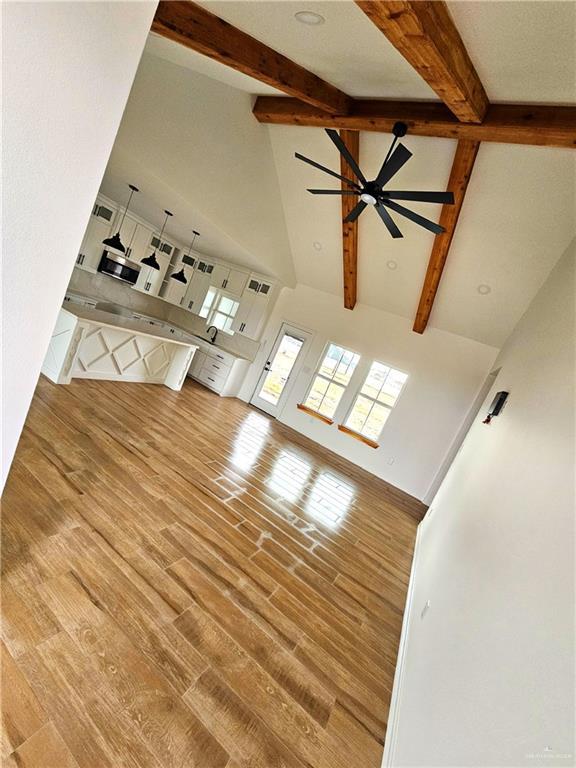 unfurnished living room with hardwood / wood-style flooring, ceiling fan, beam ceiling, and high vaulted ceiling