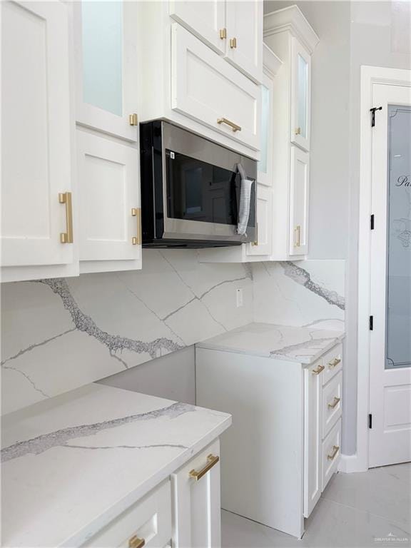 1205 Moses Dr, San Juan, TX 78589 - kitchen with stainless steel microwave, white cabinetry, light stone counters, and glass insert cabinets