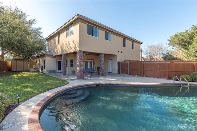 rear view of property featuring a fenced in pool, a lawn, a patio, and a storage unit