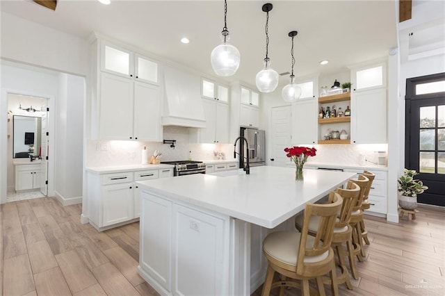 kitchen with glass insert cabinets, a kitchen island with sink, white cabinetry, and light countertops