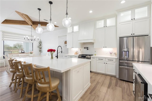 kitchen featuring stainless steel appliances, light countertops, glass insert cabinets, a kitchen island with sink, and a sink