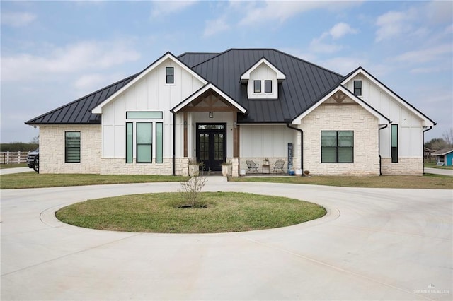 modern farmhouse style home with stone siding, curved driveway, metal roof, a standing seam roof, and board and batten siding