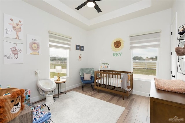 bedroom featuring light wood-type flooring, a nursery area, baseboards, and a raised ceiling