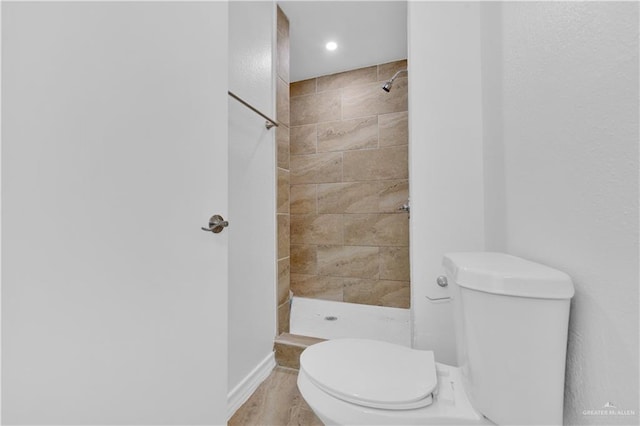 full bath with toilet, baseboards, and a tile shower