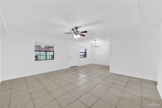 empty room featuring baseboards, light tile patterned floors, and ceiling fan with notable chandelier