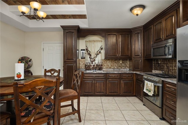 kitchen with dark brown cabinets, appliances with stainless steel finishes, an inviting chandelier, stone counters, and tasteful backsplash