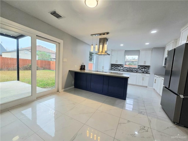 kitchen featuring decorative light fixtures, ventilation hood, white cabinetry, stainless steel fridge, and kitchen peninsula